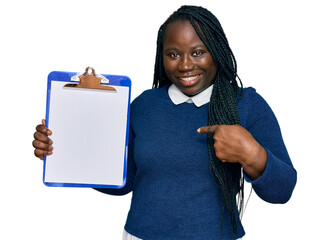 Canvas Print - Young black woman with braids holding clipboard with blank space pointing finger to one self smiling happy and proud