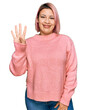 © Krakenimages.com - Hispanic woman with pink hair wearing casual winter sweater showing and pointing up with fingers number four while smiling confident and happy.