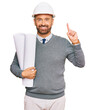 © Krakenimages.com - Handsome middle age man holding paper blueprints surprised with an idea or question pointing finger with happy face, number one