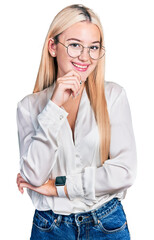 Wall Mural - Beautiful blonde woman wearing elegant shirt and glasses looking confident at the camera smiling with crossed arms and hand raised on chin. thinking positive.