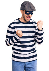 Canvas Print - Young handsome man wearing burglar mask celebrating surprised and amazed for success with arms raised and eyes closed. winner concept.