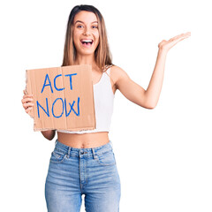 Canvas Print - Young beautiful girl holding act now banner celebrating victory with happy smile and winner expression with raised hands