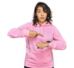 Canvas Print - Young hispanic woman wearing casual sweatshirt in hurry pointing to watch time, impatience, upset and angry for deadline delay