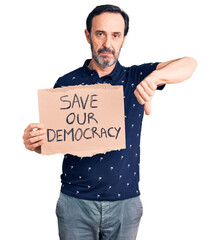 Poster - Middle age handsome man holding save our democracy cardboard banner with angry face, negative sign showing dislike with thumbs down, rejection concept