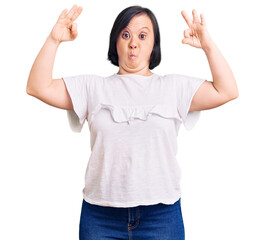 Canvas Print - Brunette woman with down syndrome wearing casual white tshirt looking surprised and shocked doing ok approval symbol with fingers. crazy expression