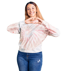 Wall Mural - Beautiful young woman wearing casual tie dye sweatshirt smiling in love showing heart symbol and shape with hands. romantic concept.