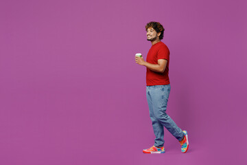 Wall Mural - Full body side view young Indian man he wear red t-shirt casual clothes hold takeaway delivery craft paper brown cup coffee to go isolated on plain purple background studio portrait Lifestyle concept