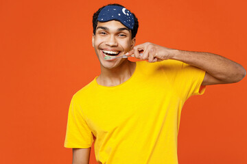 Wall Mural - Calm smiling happy cheerful young man wearing pyjamas jam sleep eye mask resting relax at home look camera brush teeth isolated on plain orange background studio portrait. Good mood night nap concept