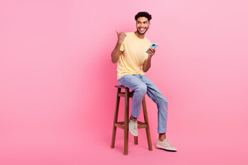 Full size photo of young guy sitting bartender direct finger novelty phone download app for friends chat isolated on pink color background