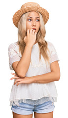 Canvas Print - Young blonde girl wearing summer hat looking stressed and nervous with hands on mouth biting nails. anxiety problem.