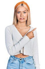 Poster - Beautiful young blonde woman wearing casual white sweater pointing aside worried and nervous with forefinger, concerned and surprised expression