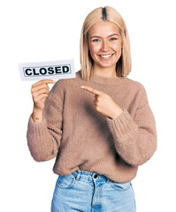 Sticker - Beautiful young blonde woman holding closed banner smiling happy pointing with hand and finger