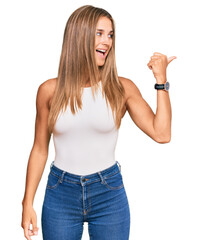 Wall Mural - Young blonde woman wearing casual style with sleeveless shirt smiling with happy face looking and pointing to the side with thumb up.