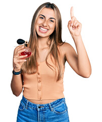 Sticker - Hispanic young woman holding perfume smiling with an idea or question pointing finger with happy face, number one