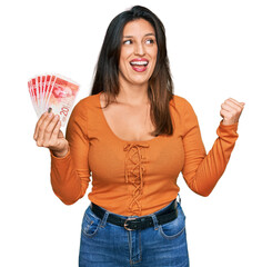 Sticker - Beautiful hispanic woman holding 20 israel shekels banknotes pointing thumb up to the side smiling happy with open mouth