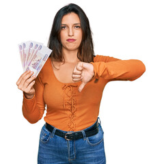 Sticker - Beautiful hispanic woman holding russian 500 ruble banknotes with angry face, negative sign showing dislike with thumbs down, rejection concept