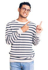 Canvas Print - Hispanic handsome young man wearing casual clothes and glasses smiling and looking at the camera pointing with two hands and fingers to the side.