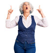 © Krakenimages.com - Senior grey-haired woman wearing casual clothes amazed and surprised looking up and pointing with fingers and raised arms.