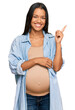 © Krakenimages.com - Beautiful hispanic woman expecting a baby showing pregnant belly smiling happy pointing with hand and finger to the side
