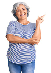 Canvas Print - Senior woman with gray hair wearing casual striped clothes with a big smile on face, pointing with hand and finger to the side looking at the camera.