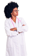 Poster - Young african american woman wearing doctor coat and stethoscope looking to the side with arms crossed convinced and confident