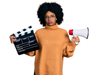 Sticker - Young african american woman holding video film clapboard and megaphone relaxed with serious expression on face. simple and natural looking at the camera.