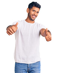 Sticker - Young latin man wearing casual clothes approving doing positive gesture with hand, thumbs up smiling and happy for success. winner gesture.