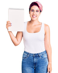 Sticker - Young beautiful woman with pink hair holding notebook looking positive and happy standing and smiling with a confident smile showing teeth