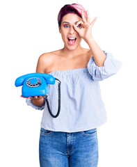 Canvas Print - Young beautiful woman with pink hair holding vintage telephone smiling happy doing ok sign with hand on eye looking through fingers