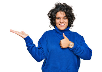 Canvas Print - Young hispanic woman with curly hair wearing turtleneck sweater showing palm hand and doing ok gesture with thumbs up, smiling happy and cheerful