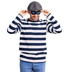 Poster - Young handsome man wearing burglar mask smiling pulling ears with fingers, funny gesture. audition problem