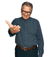 Poster - Middle age indian man wearing casual clothes and glasses smiling friendly offering handshake as greeting and welcoming. successful business.