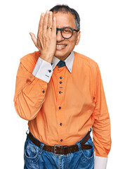 Canvas Print - Middle age indian man wearing casual clothes and glasses covering one eye with hand, confident smile on face and surprise emotion.