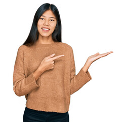 Poster - Beautiful young asian woman wearing casual winter sweater amazed and smiling to the camera while presenting with hand and pointing with finger.