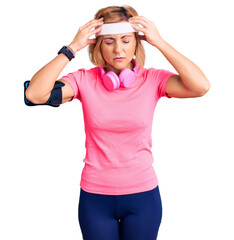 Wall Mural - Young blonde woman wearing sportswear and headphones suffering from headache desperate and stressed because pain and migraine. hands on head.