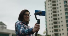 Adult Woman With Glasses Holds Gimbal Stabilizer With Blue Mobile Phone In Portrait Mode. Slow Motion Low Angle
