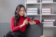 © kamiphotos - Asian beautiful woman sits in living room, she is college student listening to relaxing music, studying from home, online learning. University student concept.