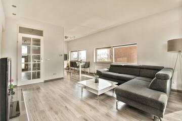 a living room with wood flooring and white walls, there is a black couch in the center of the room