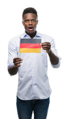 Poster - Young african american man holding german flag scared in shock with a surprise face, afraid and excited with fear expression