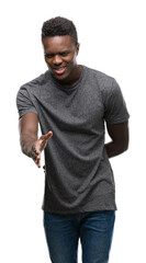 Poster - Young african american man wearing grey t-shirt smiling friendly offering handshake as greeting and welcoming. Successful business.