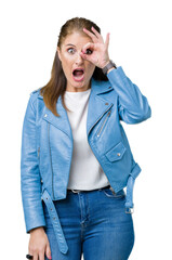 Sticker - Beautiful middle age mature woman wearing fashion leather jacket over isolated background doing ok gesture shocked with surprised face, eye looking through fingers. Unbelieving expression.