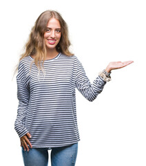 Poster - Beautiful young blonde woman wearing stripes sweater over isolated background smiling cheerful presenting and pointing with palm of hand looking at the camera.