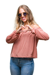 Poster - Beautiful young blonde woman wearing retro sunglasses over isolated background smiling in love showing heart symbol and shape with hands. Romantic concept.