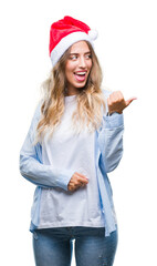 Sticker - Beautiful young blonde woman wearing christmas hat over isolated background smiling with happy face looking and pointing to the side with thumb up.