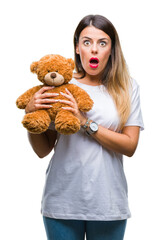 Wall Mural - Young beautiful woman holding teddy bear plush over isolated background scared in shock with a surprise face, afraid and excited with fear expression