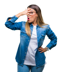 Canvas Print - Young beautiful woman over wearing glasses over isolated background peeking in shock covering face and eyes with hand, looking through fingers with embarrassed expression.