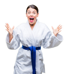 Canvas Print - Young beautiful woman wearing karate kimono uniform over isolated background celebrating crazy and amazed for success with arms raised and open eyes screaming excited. Winner concept