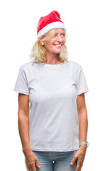 Sticker - Middle age blonde woman wearing christmas hat over isolated background looking away to side with smile on face, natural expression. Laughing confident.