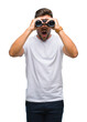 © Krakenimages.com - Young handsome man looking through binoculars over isolated background scared in shock with a surprise face, afraid and excited with fear expression