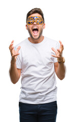 Wall Mural - Young handsome man wearing carnival mask over isolated background crazy and mad shouting and yelling with aggressive expression and arms raised. Frustration concept.